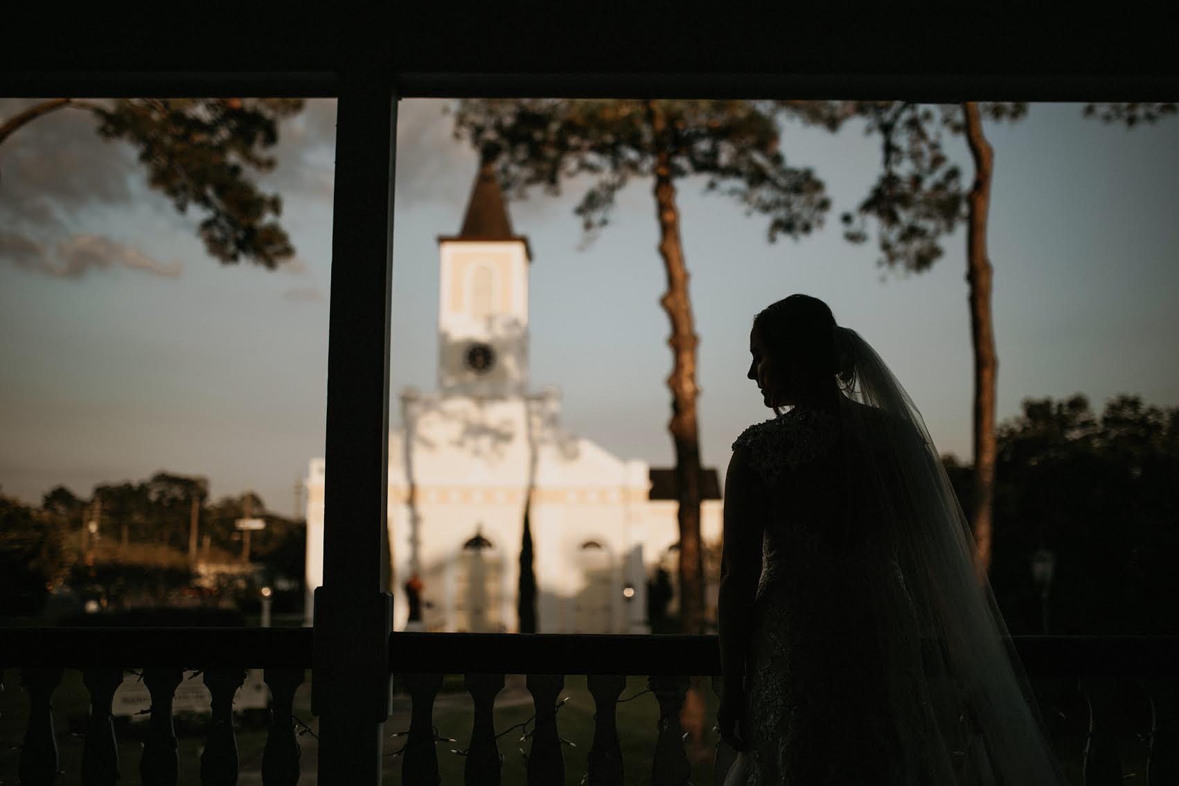 Bride silhouette on balcony overlooking Saint Martin De Tours Catholic Church at Maison De Tours historic venue Saint Martinville Louisiana
